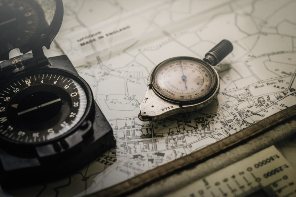 A lensatic compass, a pocket altimeter and a scale rule lying on a folded topographic map
